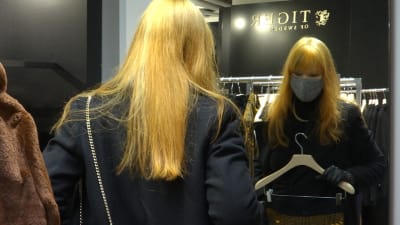 En kvinna poserar med ett plagg i hand framför en spegel i en affär. 