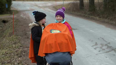 Två flickor går längs en landsväg med en barnvagn.