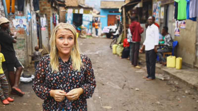 En blond kvinna står på en lerig gata i Uganda.