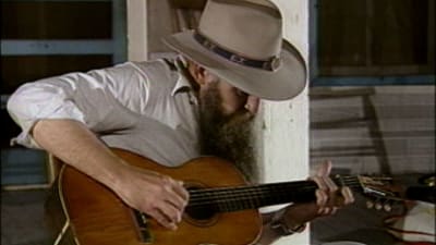 Blaze Foley istuu ja soittaa kitaraa cowboyhattu päässä