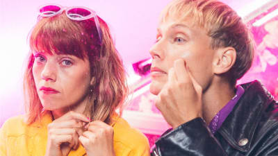 Oona (Anna Airola) ja Arttu (Elias Salonen) vierekkäin lähikuvassa pinkkiä taustaa vasten.