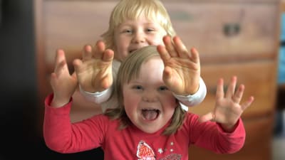 Två småbarn med ljust hår ler och visar sina händer åt kameran.