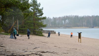 Folk städar på simstrand i regnigt väder. 