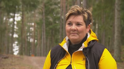 Petra Mannström, en dam med kort hår och gul jacka, står i en skog.