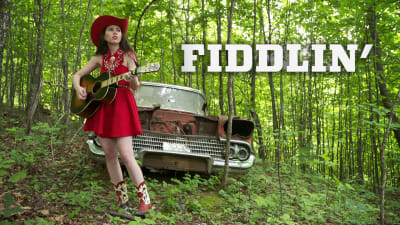 Nuori nainen cowboybootseissa ja -hatussa kitara kädessä mets'ss, kuvan päällä otsikko Fiddlin'.