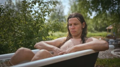Alaston mies (taiteilija Antti Laitinen) istuu kylvyssä ammeessa, joka on pihamaalla.