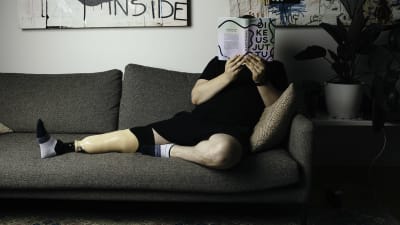 Jalkaproteesin omaava mies istuu sohvalla ja lukee kirjaa.