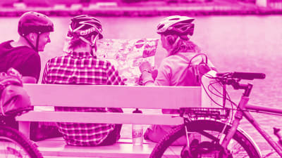 Pyöräilijät istuvat penkillä tutkimassa paperikarttaa.