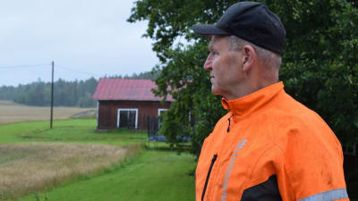 Peter Lindström, iförd orange arbetshalare, ser ut över åkrarna i regnigt augustiväder.