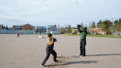 En person håller på att svinga ett bobollsträ och en annan slänger boll i luften. 
