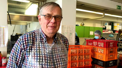 en man i glasögon och rutig skjorta i en sal där man packeterar matvaror