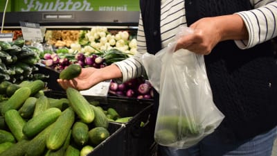 En kvinna plockar gurka i sin påse i matbtutiken.