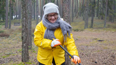 Minna Söderholm i gul regnjacka i en skog med en kratta i händerna. 