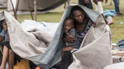 En kvinna och ett barn tar skydd under presenning i Haiti.