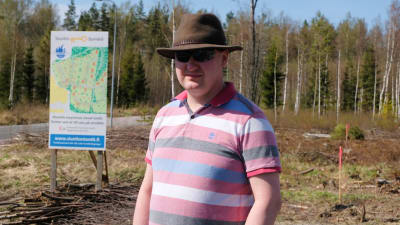 En medelåldersman i hatt och solglasögon som står vid en tom tomt. 