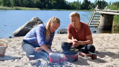 Två personer lagar mat på stranden.