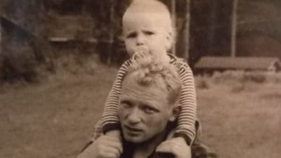 Ett svartvitt fotografi på en man som bär en pojke på sina axlar.