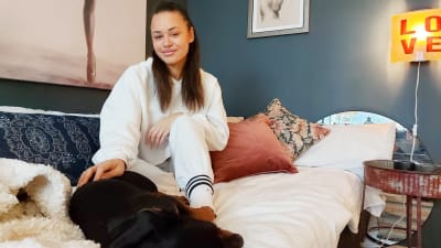 Kiara Nelson på säng med hund. Tavlor på väggen