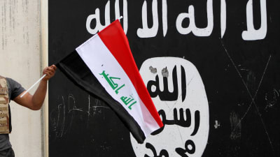 En hand som håller i Iraks flagga framför en svartvit IS flagga.