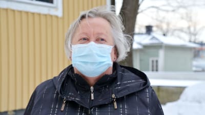 Birgitta Lindén utomhus framför en gul byggnad med munskydd på. 