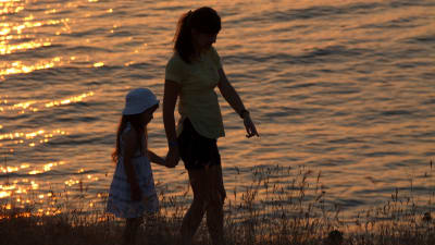 kvinna och liten flicka går på stranden i kvällssolen