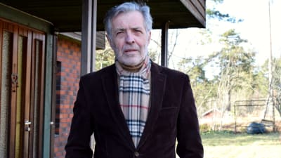 Jan-Erik Enestam i brun tweed-kavaj utanför ett tegelhus.