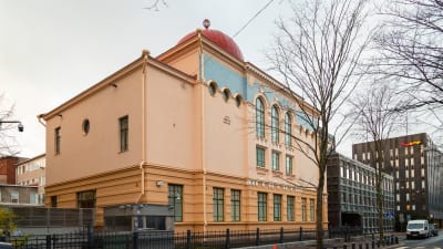 Gatuvy över Helsingfors synagoga - ett gult hus i klassisk stil, ett rött kupoltak skymtas där ett tak ska vara.