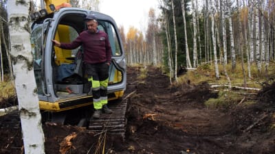 Grävmaskin intill nyligen igengrävt dike i en björkskog.