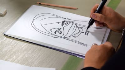 En hand håller i en svart tuschpenna och ritar en seriefigur som föreställer en kvinnlig ninja.