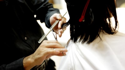 En frisörs händer som klipper ett mörkt axellångt hår