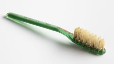 Gammal tandborste med skaft av grönt plast.