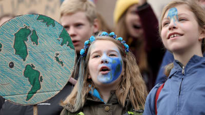 Unga demonstrerar för klimatet på riksdagshusets trappor i Helsingfors.