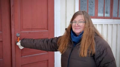 Lilian Petterson-Smeds står framför Svedbergska skolan i Munsala. Dörren är röd och hon är på väg att öppna den.