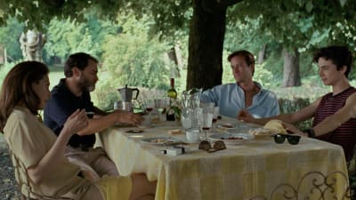 Familjen Perlman och Oliver (Armie Hammer) sitter vid ett bord utomhus, under ett träd och äter.