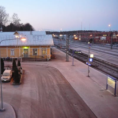 En gammal gul järnvägsstation, järnvägsspår, parkerade bilar med isiga vindrutor. Skymning.