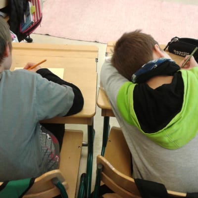 Kaksi alakoululaista poikaa on kumpartunut pulpettinsa ylle kirjoitustehtävään.