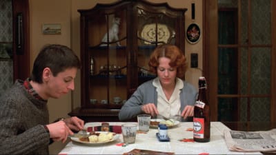 Nainen ja nuori mies syövät ruokapöydän ääressä. Kuva elokuvasta Jeanne Dielman.