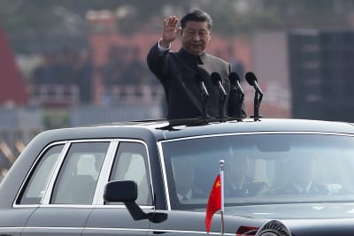 Kinas president Xi Jinping står upp i takluckan till sin limousin och gör en hälsningsrörelse.