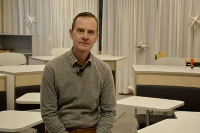 Mikael Fröjdö sitter på en stol i en modern lärmiljö med bord som är ordnade som en hästsko i rummet.