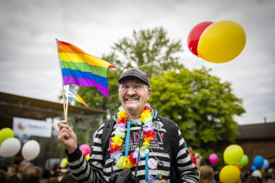 Leveästi hymyilevä mies heiluttaa sateenkaarilippua pridessa.