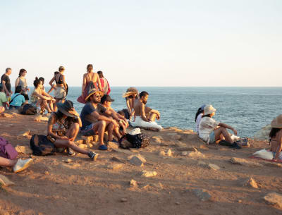 Turisteja istuskelemasssa ilta-auringossa hiekarannalla