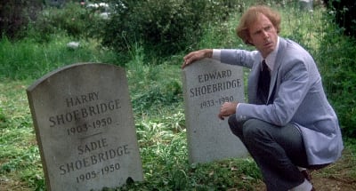 Mies (näyttelijä Bruce Dern) nojaa ihmettelevän näköisenä hautakiveen, jonka vieressä on toinen; molemmissa kivissä on sama sukunimi ja kuolinvuosi, mutta toinen on vanha ja toinen upouusi. Kuva Hitchcockin elokuvasta Perintö.