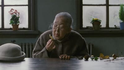 Vanha japanilainen nainen istuu pöydän ääressä, kuva elokuvasta Elämän jälkeen.