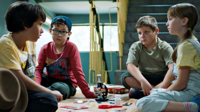 Fyra barn sitter på ett bord och ser på varandra i serien Zoki Poki.
