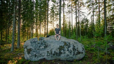 Niilo issakainen istuu kivellä metsässä.