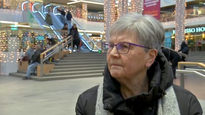 Äldre kvinna i glasögon i ett köpcentrum.