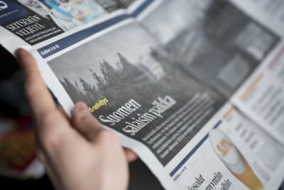 En person håller i en Helsingin Sanomat-tidning.