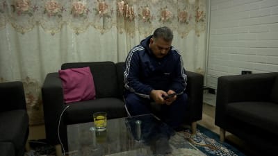 En man sitter i en soffa och bläddrar i sin telefon