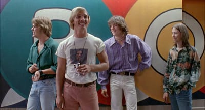 Neljä nuorta poikaa tai miestä 1970-luvun tyylisissä vaatteissa seisoo rennosti hymyillen, etualan tyypillä kädessään oluttölkki, taustalla kirjava seinä, kuva elokuvasta Surutta? Sekaisin.