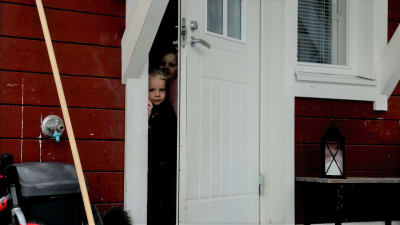 Två barn tittar ut genom dörrspringa.